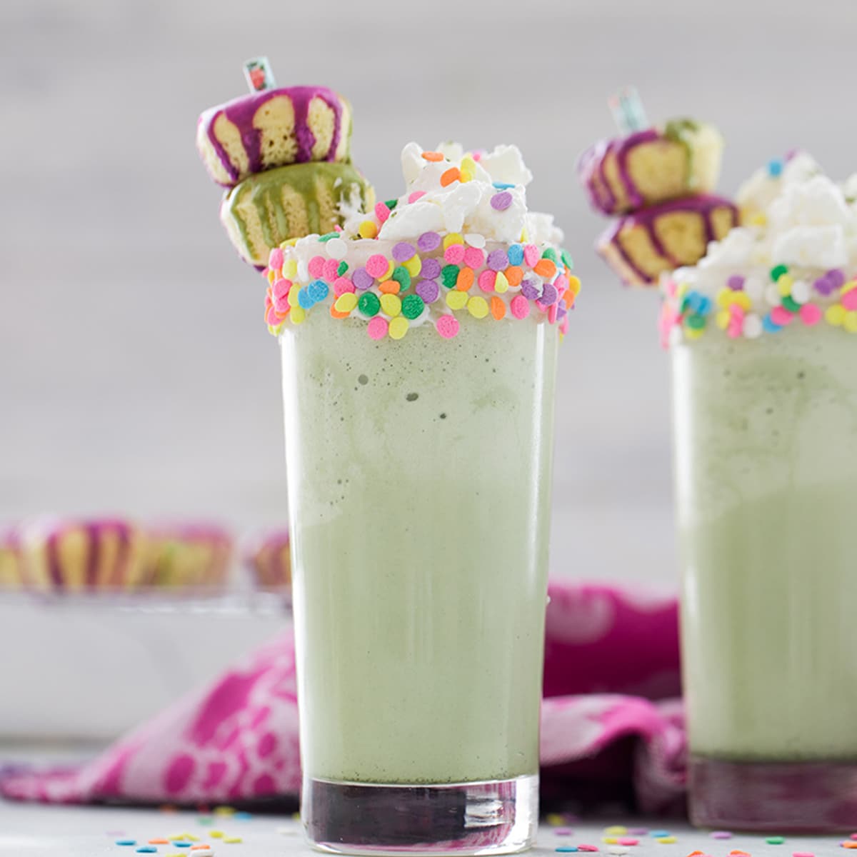 Head-on view of two matcha milkshakes with sprinkles and mini donuts.