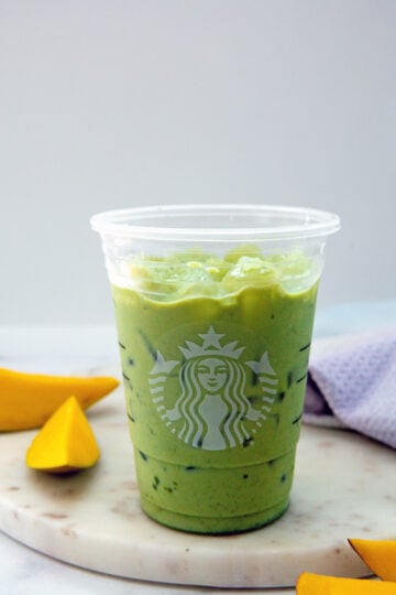Iced matcha mixed with milk and syrup in Starbucks cup with sliced mango all around.