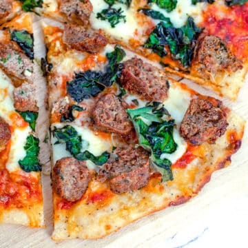 Closeup view of a meatball pizza with kale, red sauce, and cheese.