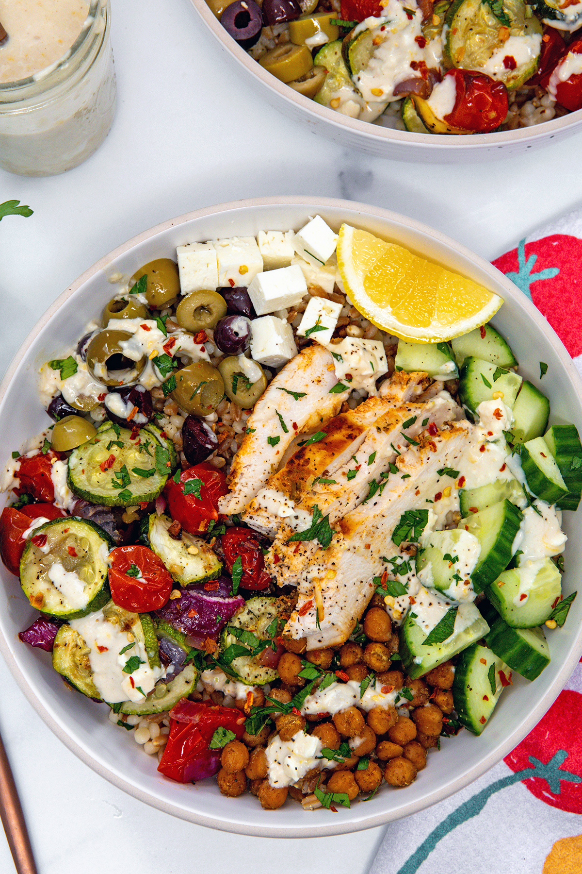 Overhead closeup view of a Mediterranean grain bowl with chicken and lots of veggies and a lemon wedge.