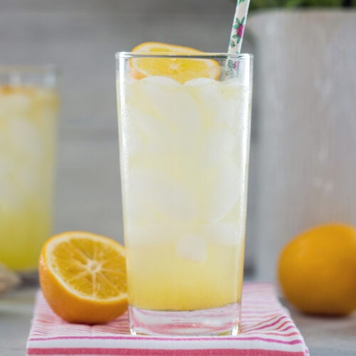 Closeup view of a Meyer Lemon Tom Collins cocktail with Meyer lemon wedges in the background.