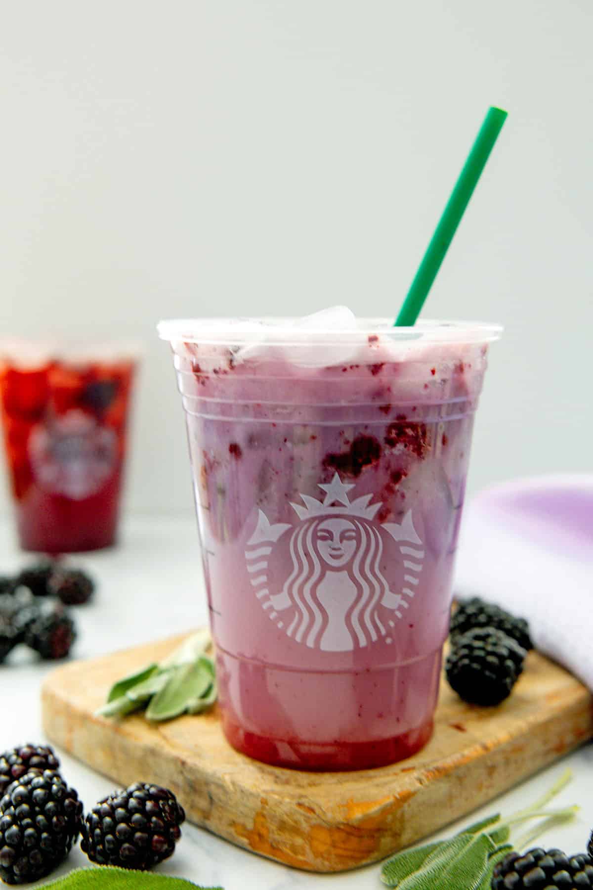 Midnight Drink in a Starbucks cup with a green straw with Blackberry Sage Refresher in background and blackberries and sage leaves all around.