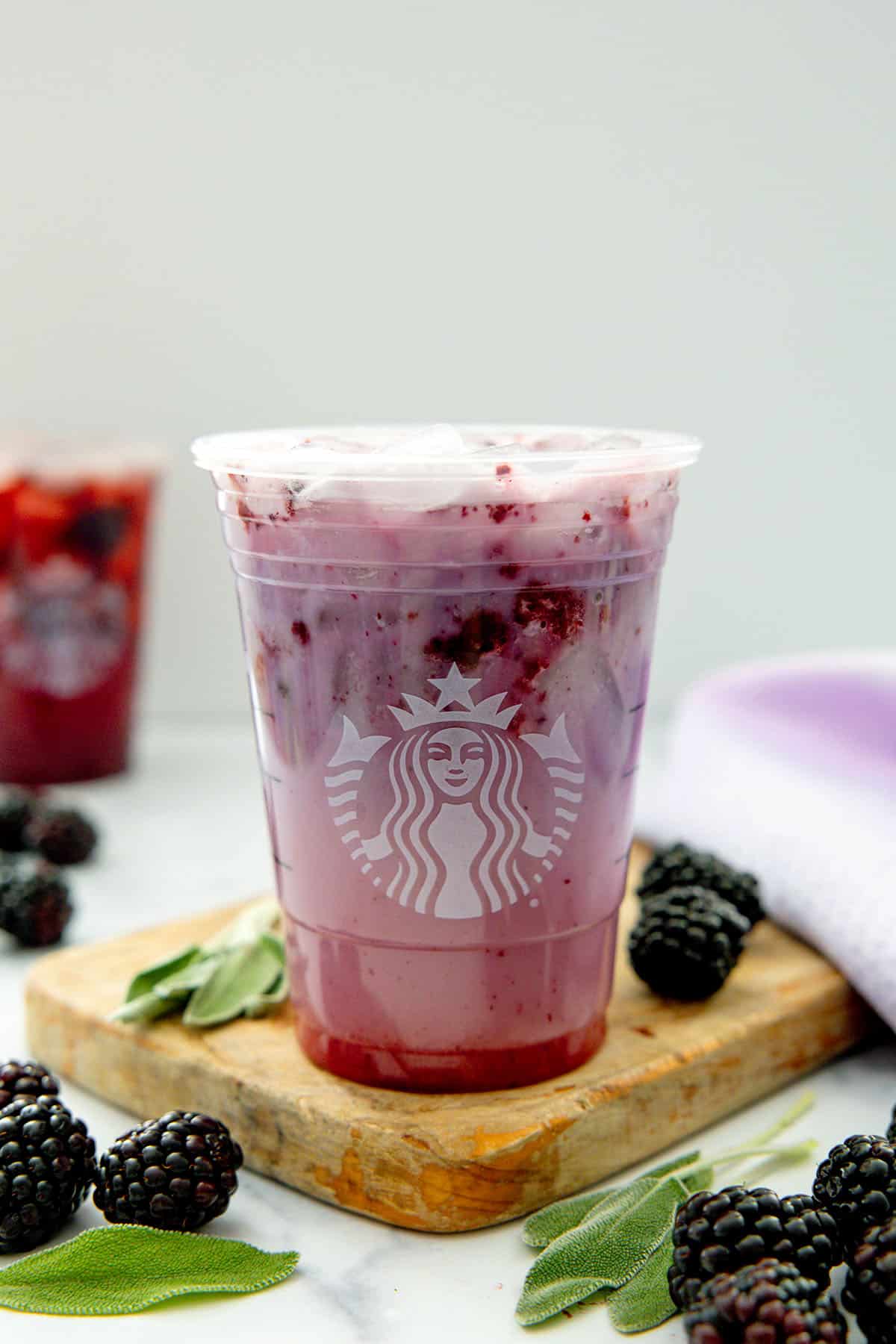 Head-on view of the Midnight Drink in a Starbucks cup with blackberries and sage all around.
