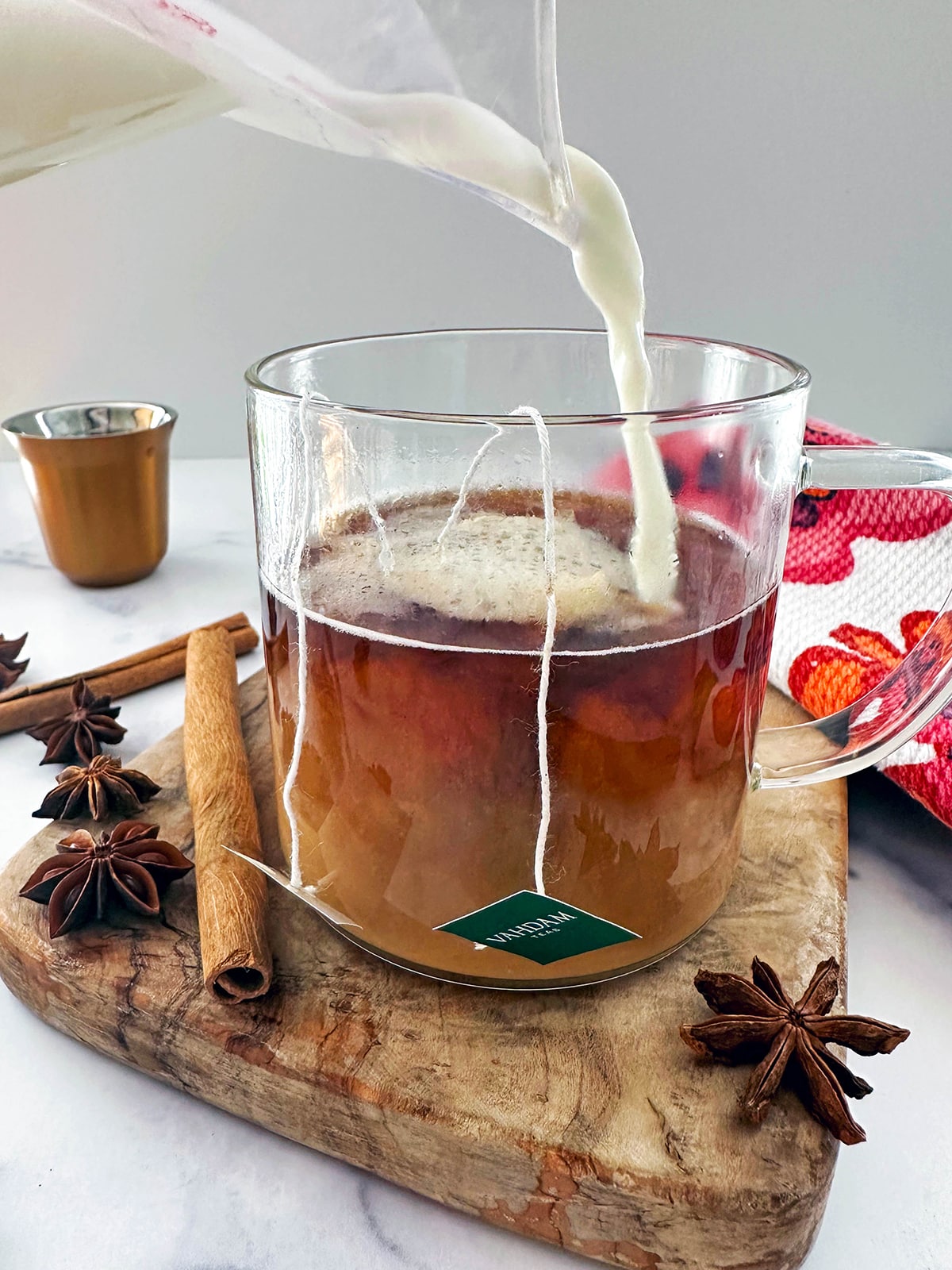 Steamed milk being poured into glass mug of chai tea and espresso.