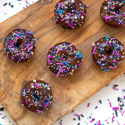 Close-up of mini chocolate donuts on a wooden board with sprinkles all around.