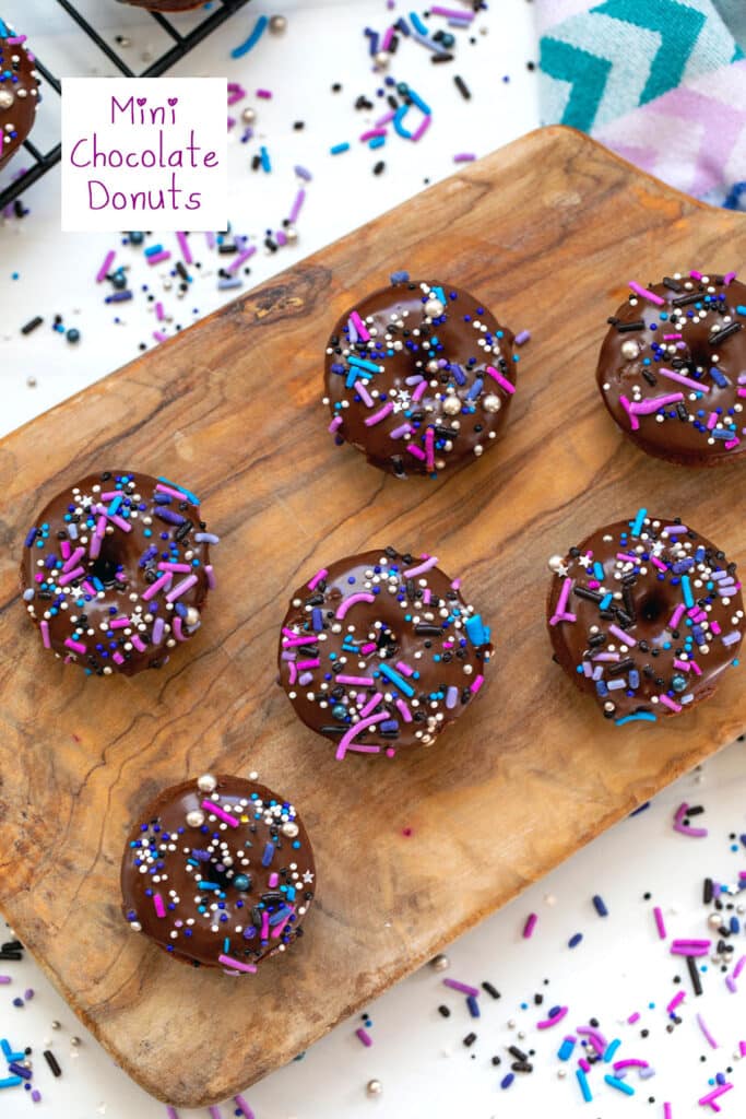 Mini chocolate donuts on a wooden cutting board with sprinkles all around and recipe title at top.