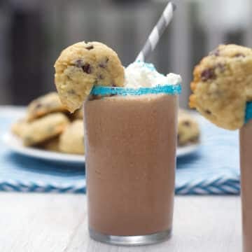Closeup head-on view of a small chocolate milkshake with mini cookie garnish and straw.