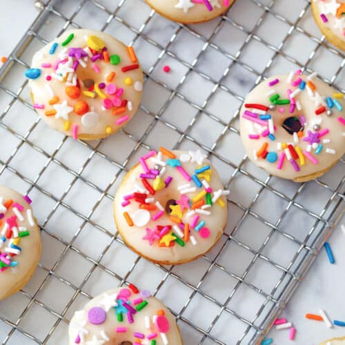 Mini donuts with colorful sprinkles on a baking rack.