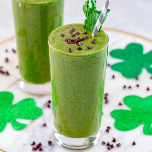 Closeup view of a mint chocolate green smoothie with mini chocolate chips and green shamrocks in background.