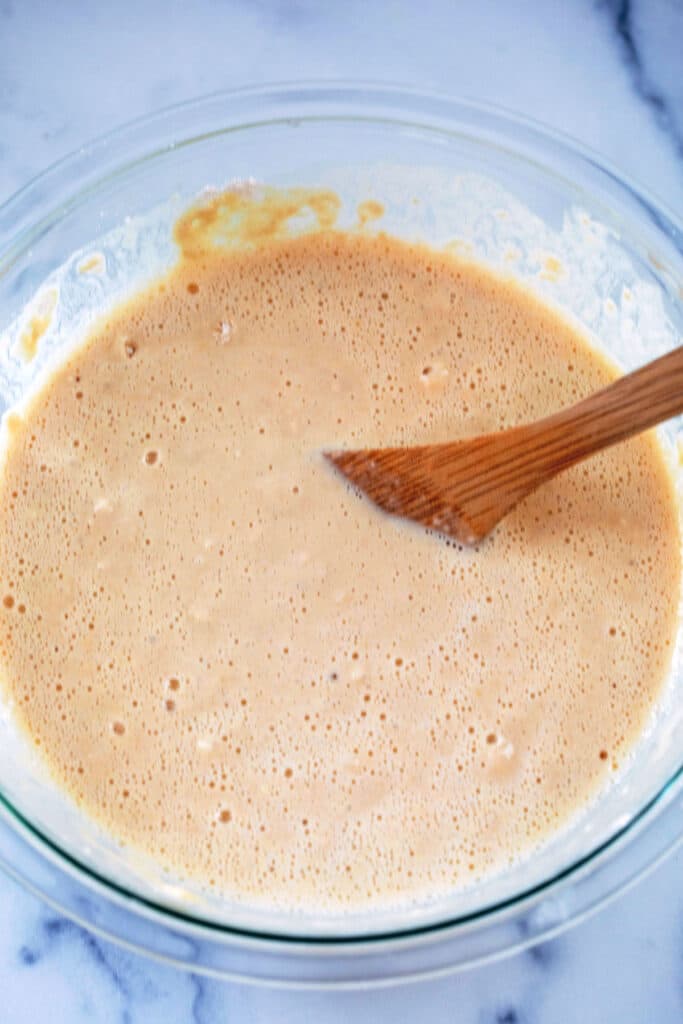 Pancake batter in mixing bowl with wooden spoon.