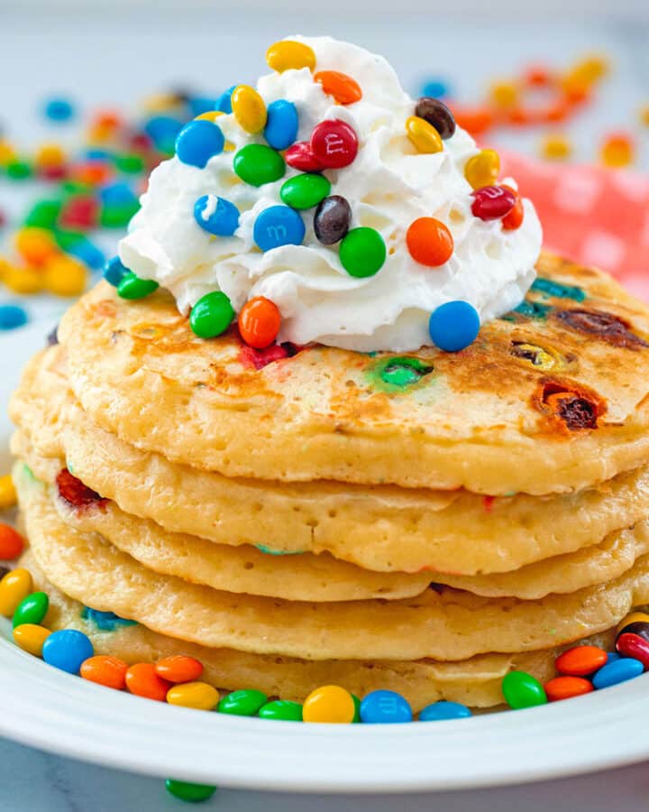 Head-on view of a stack of M&M pancakes topped with whipped cream and mini M&Ms.