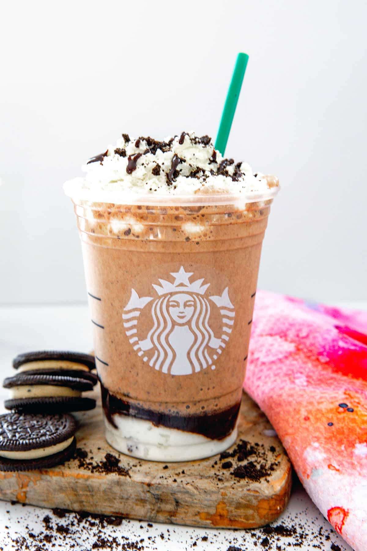 Mocha Cookie Crumble Frappuccino in Starbucks cup with green straw and Oreo cookies and crumbs around.