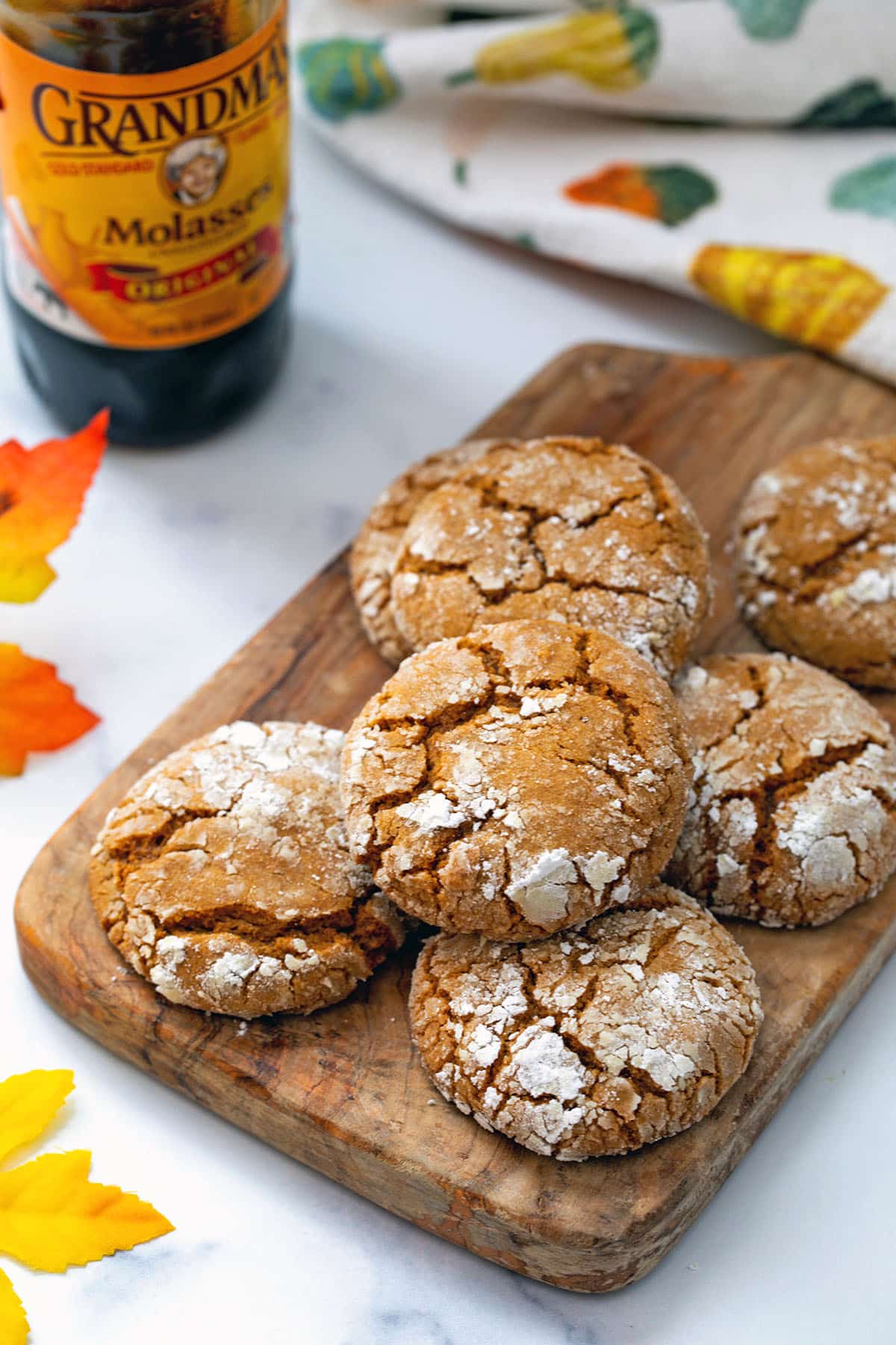 Molasses crinkle cookies on wooden board with container of molasses and fall leaves in background.