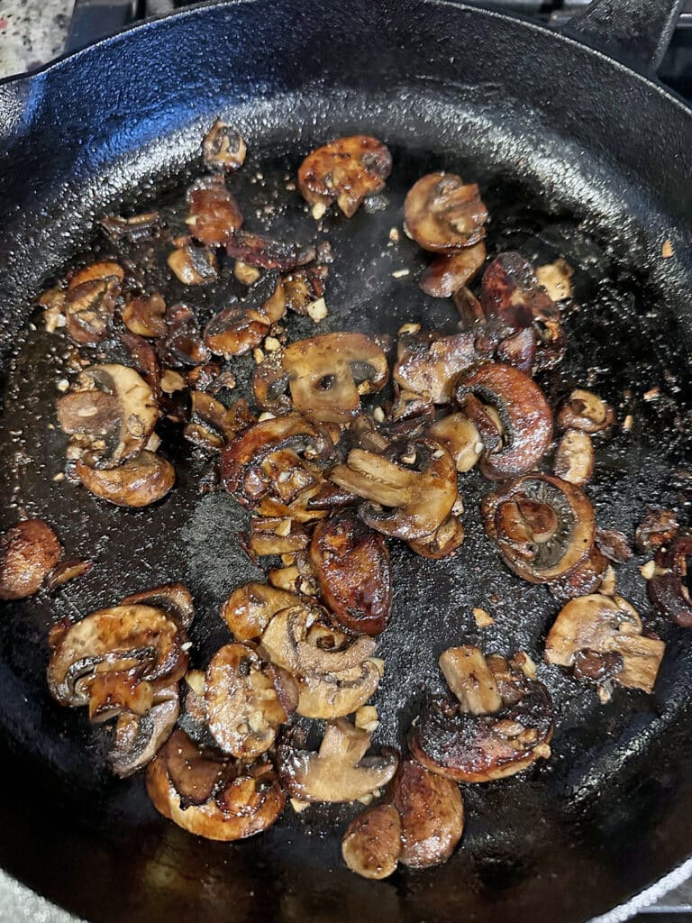Mushrooms caramelizing in cast iron skillet with garlic.