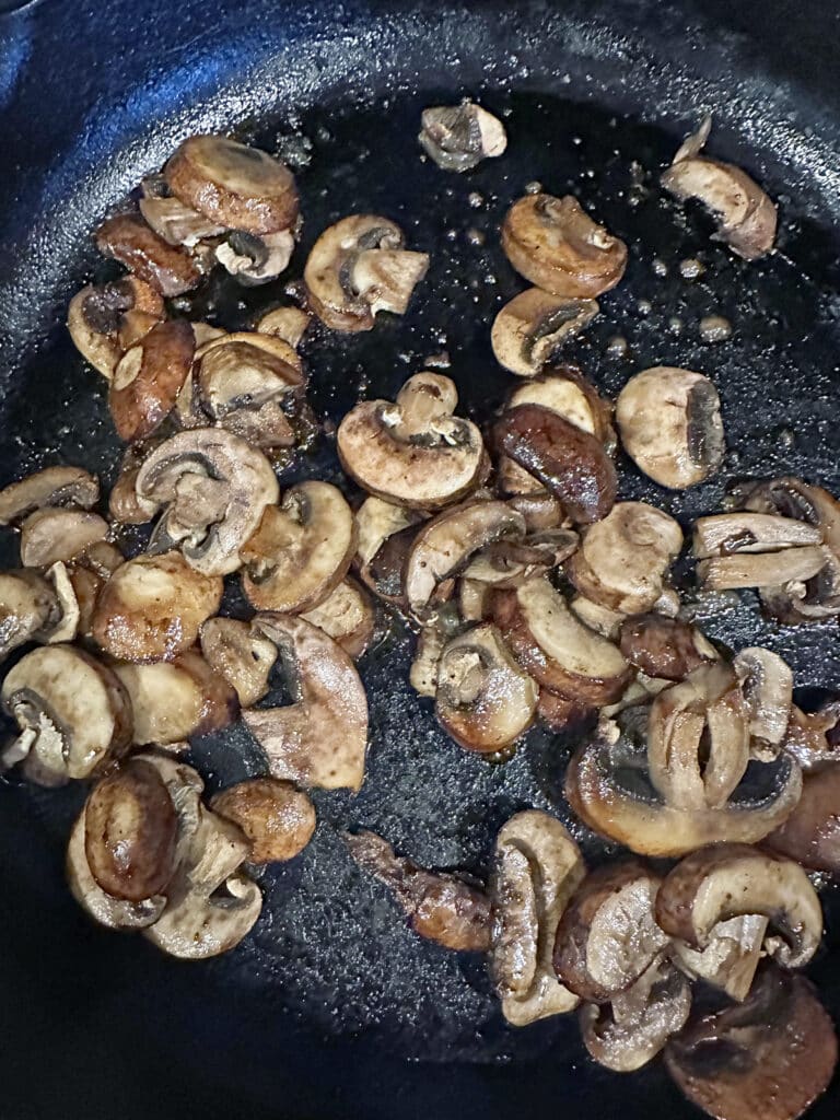 Mushrooms starting to cook in cast iron skillet.