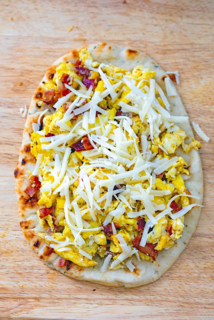 Scrambled eggs, crumbled bacon, and shredded cheese on naan round.