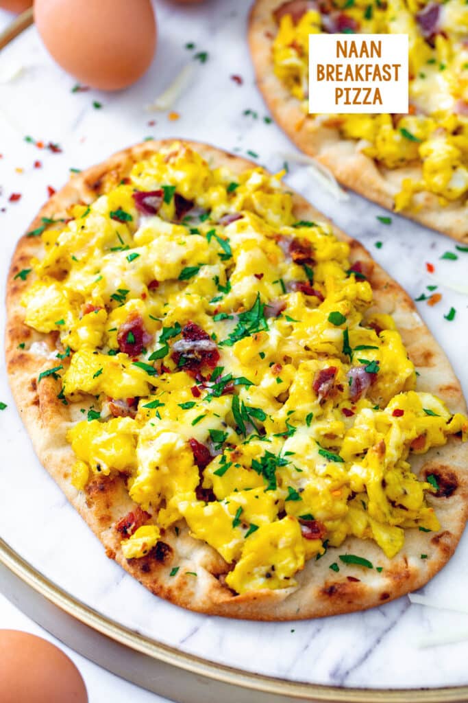 Naan breakfast pizza with scrambled eggs, bacon, and parsley with second pizza and whole eggs in background and recipe title at top.