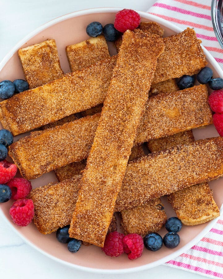 Overhead closeup view of cinnamon sugar naan french toast sticks on a plate surrounded by blueberries and raspberries.