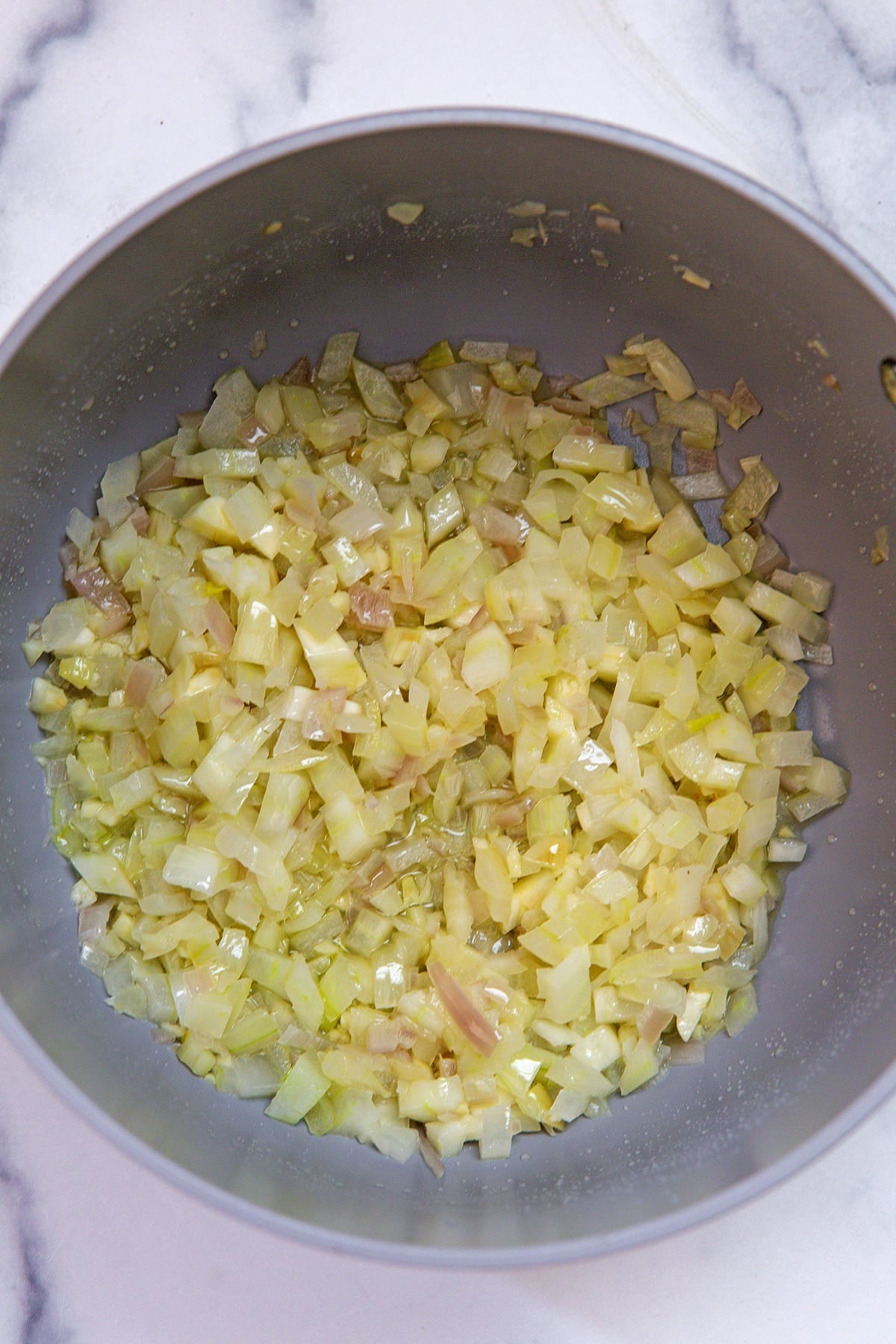 Overhead view of onions and garlic cooking in a saucepan.
