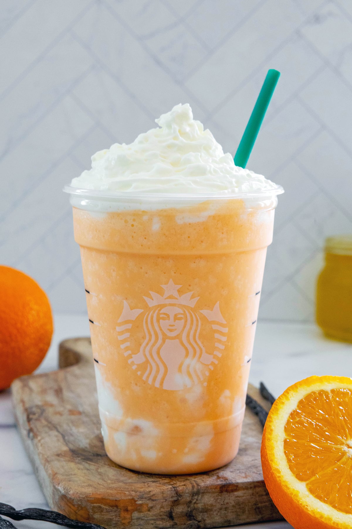 Head-on view of an Orange Frappuccino in a Starbucks cup with oranges all around.