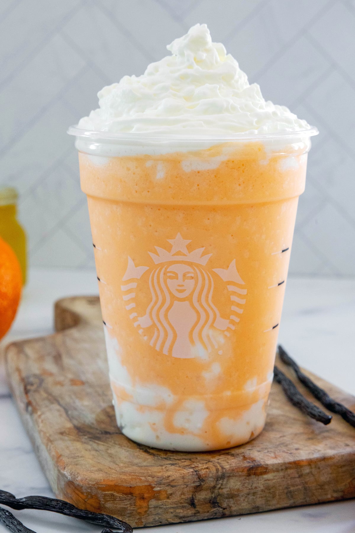 Head-on view of an Orange Cream Frappuccino topped with whipped cream with vanilla beans all around.