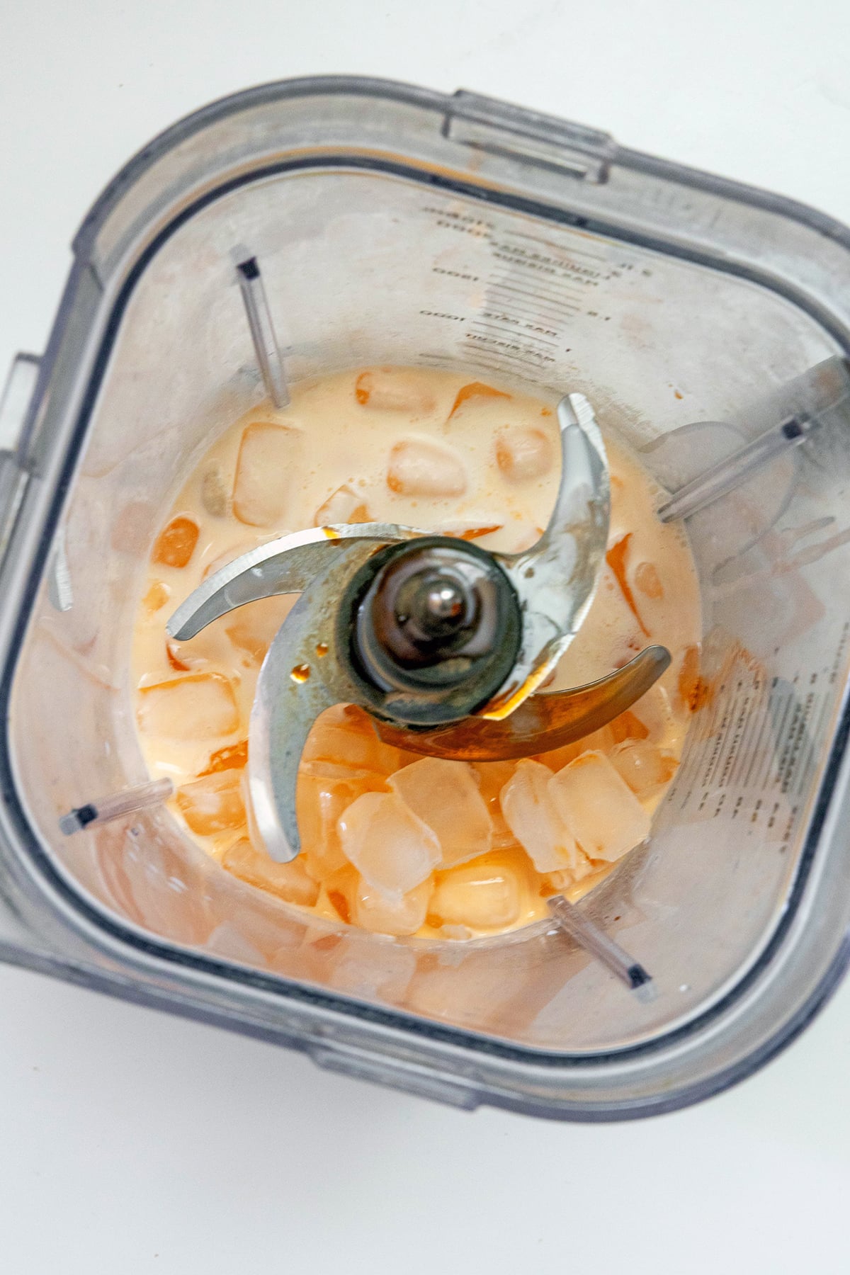 Overhead view of blender with ice, milk, cream, orange syrup, and vanilla syrup.