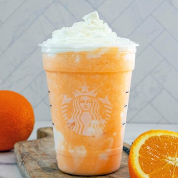 Closeup view of an Orange Cream Frappuccino in a Starbucks cup with sliced orange and whole orange.
