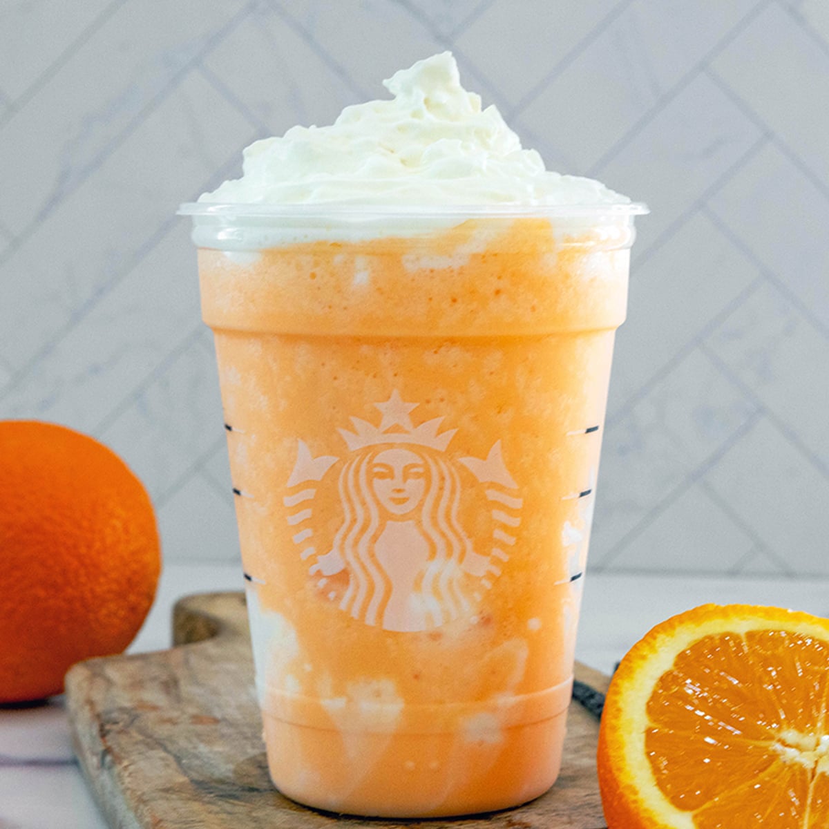 Closeup view of an Orange Cream Frappuccino in a Starbucks cup with sliced orange and whole orange.