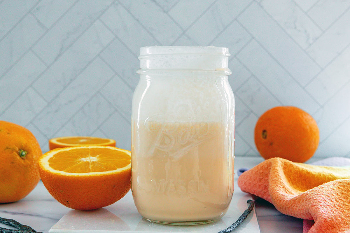 Landscape head-on view of a mason jar of orange cream sweet cream with fresh oranges all around.