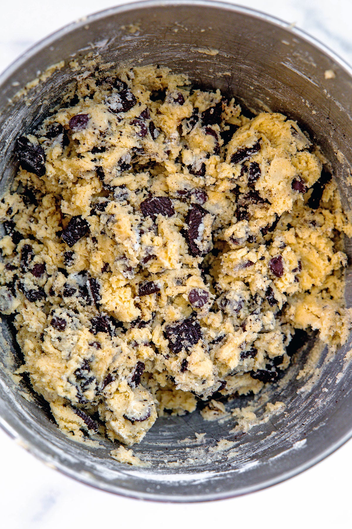 Cookie dough with chocolate chips and chopped Oreo cookies in mixing bowl.