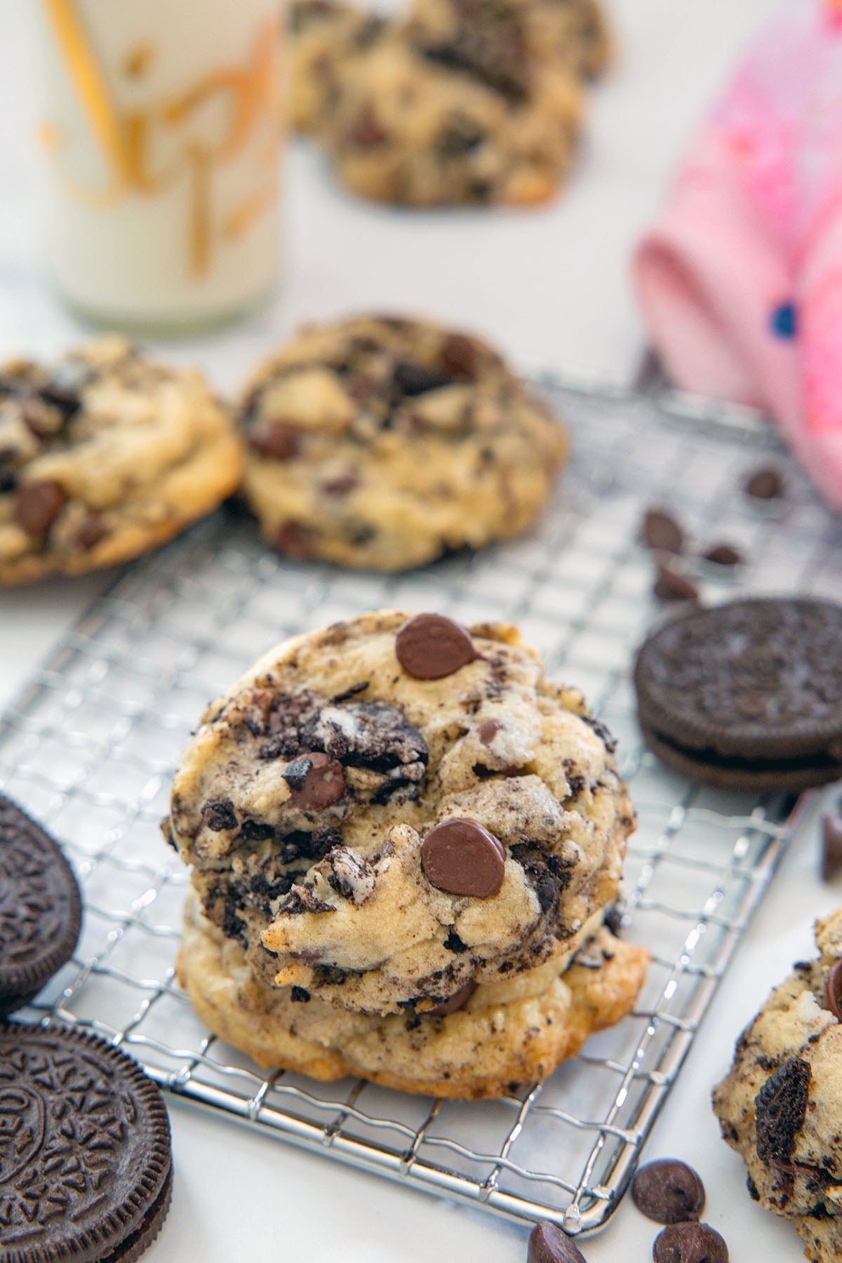 Stack of Oreo chocolate chip cookies with more in the background, along with carafe of milk.