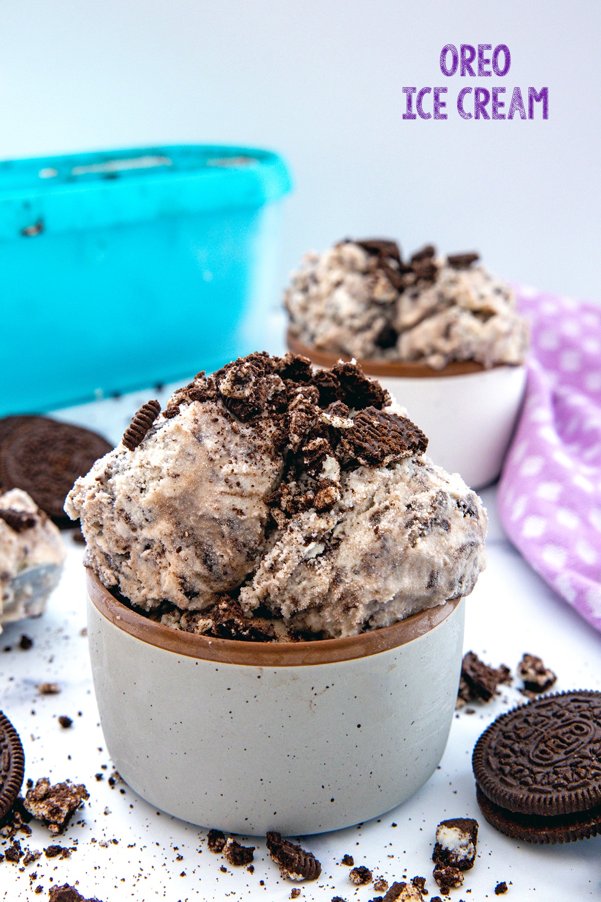 Head-on view of a bowl of Oreo ice cream with second bowl and container in background, Oreo cookies all around and recipe title at top.
