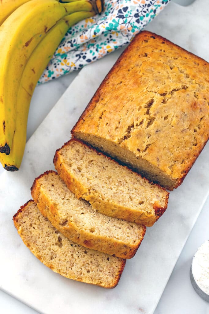 Overhead view of loaf of pancake mix banana bread with some slices cut out with bananas on the side.