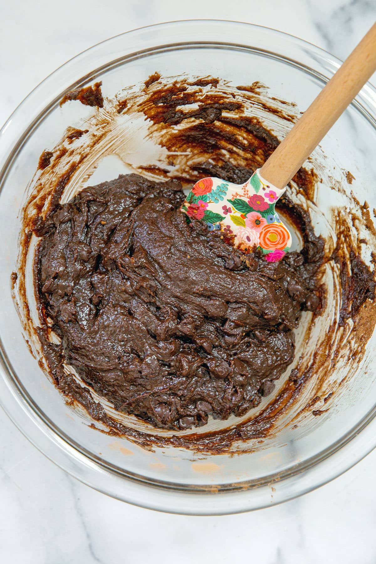 Overhead view of chocolate brownie batter in bowl with spatula.