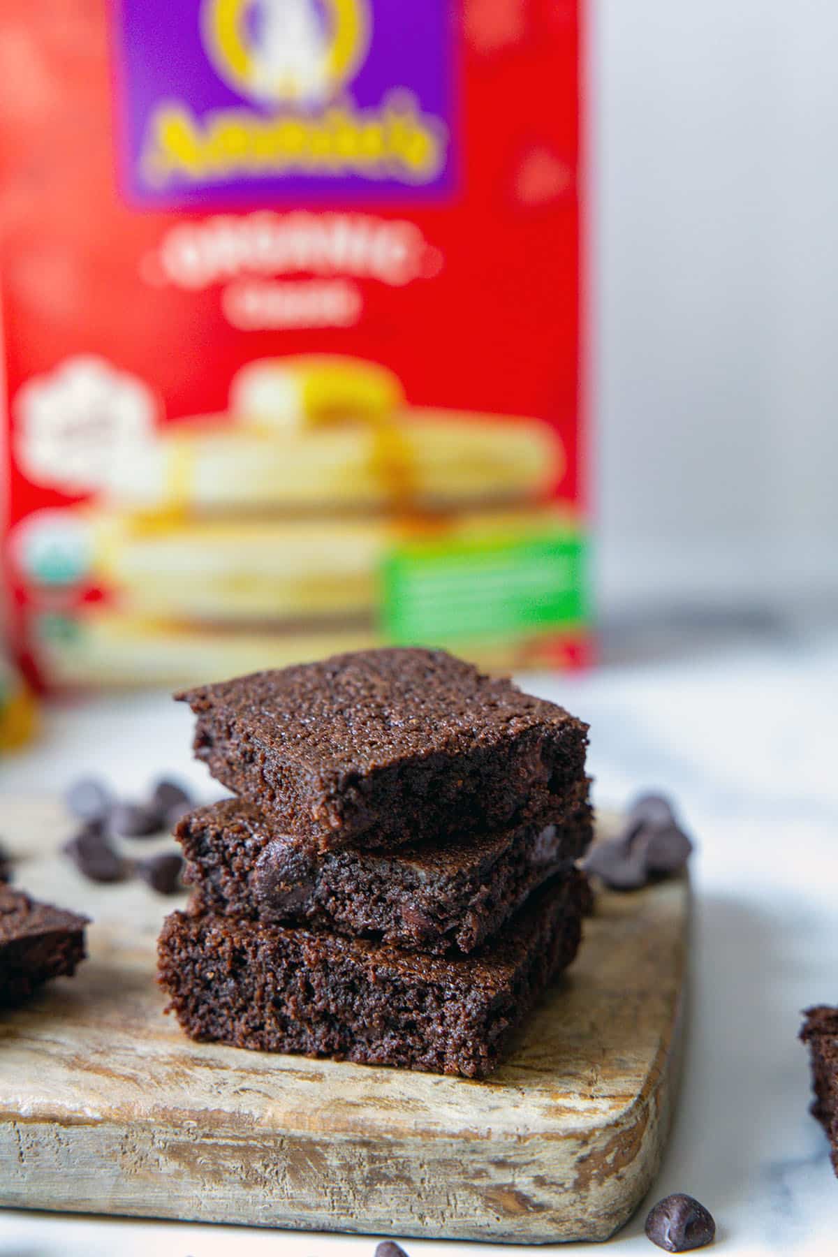 Closeup stack of chocolate brownies with box of pancake mix in background and chocolate chips all around.