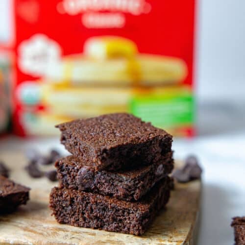 Closeup view of a stack of chocolate brownies with box of pancake mix in background.