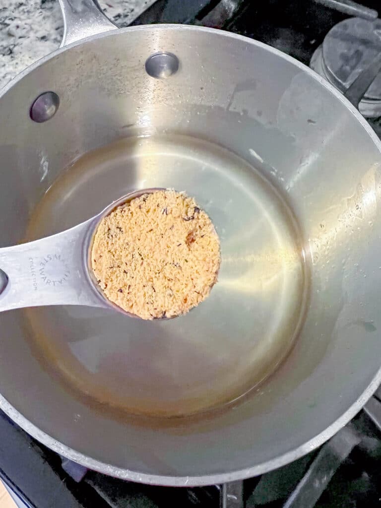 Passionfruit powder in teaspoon being added to syrup in saucepan.
