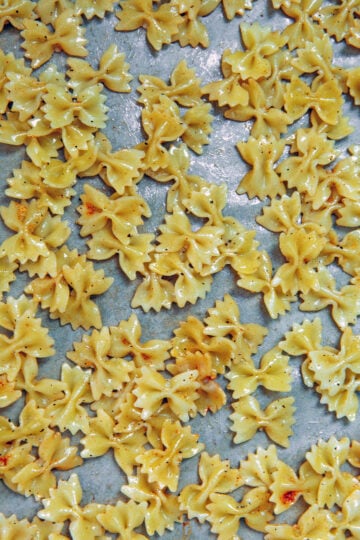 Mini bowtie pasta tossed in olive oil on a baking sheet.