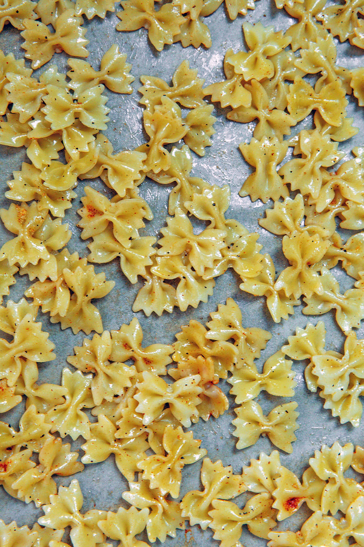 Mini bowtie pasta tossed in olive oil on a baking sheet.