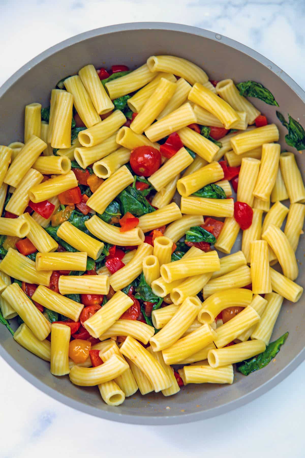 Pasta in saucepan with tomatoes, peppers, and spinach.
