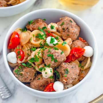 Closeup view of a bowl o pasta with turkey meatballs and mozzarella balls.