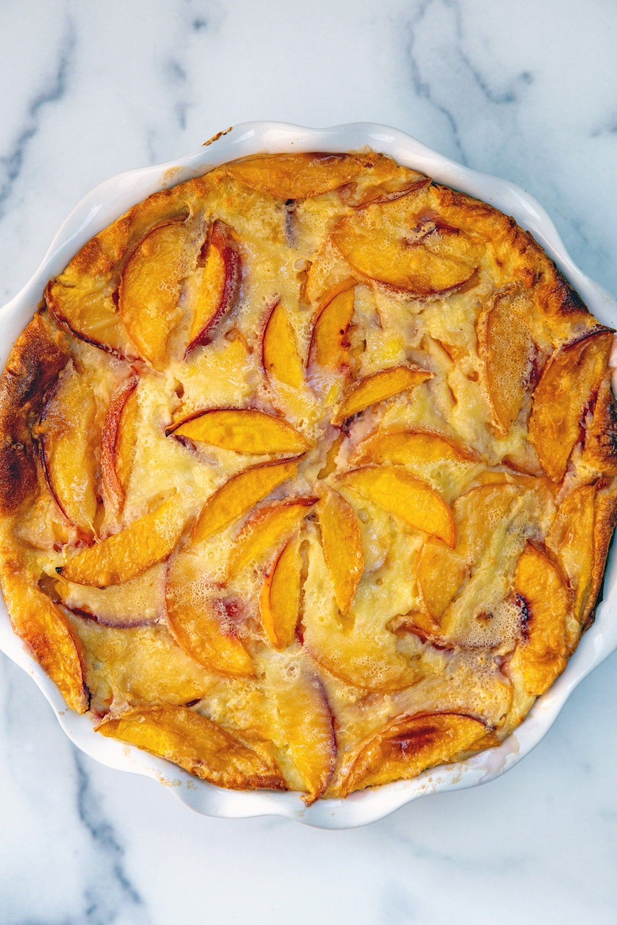 Overhead view of baked peach clafoutis in pie dish.