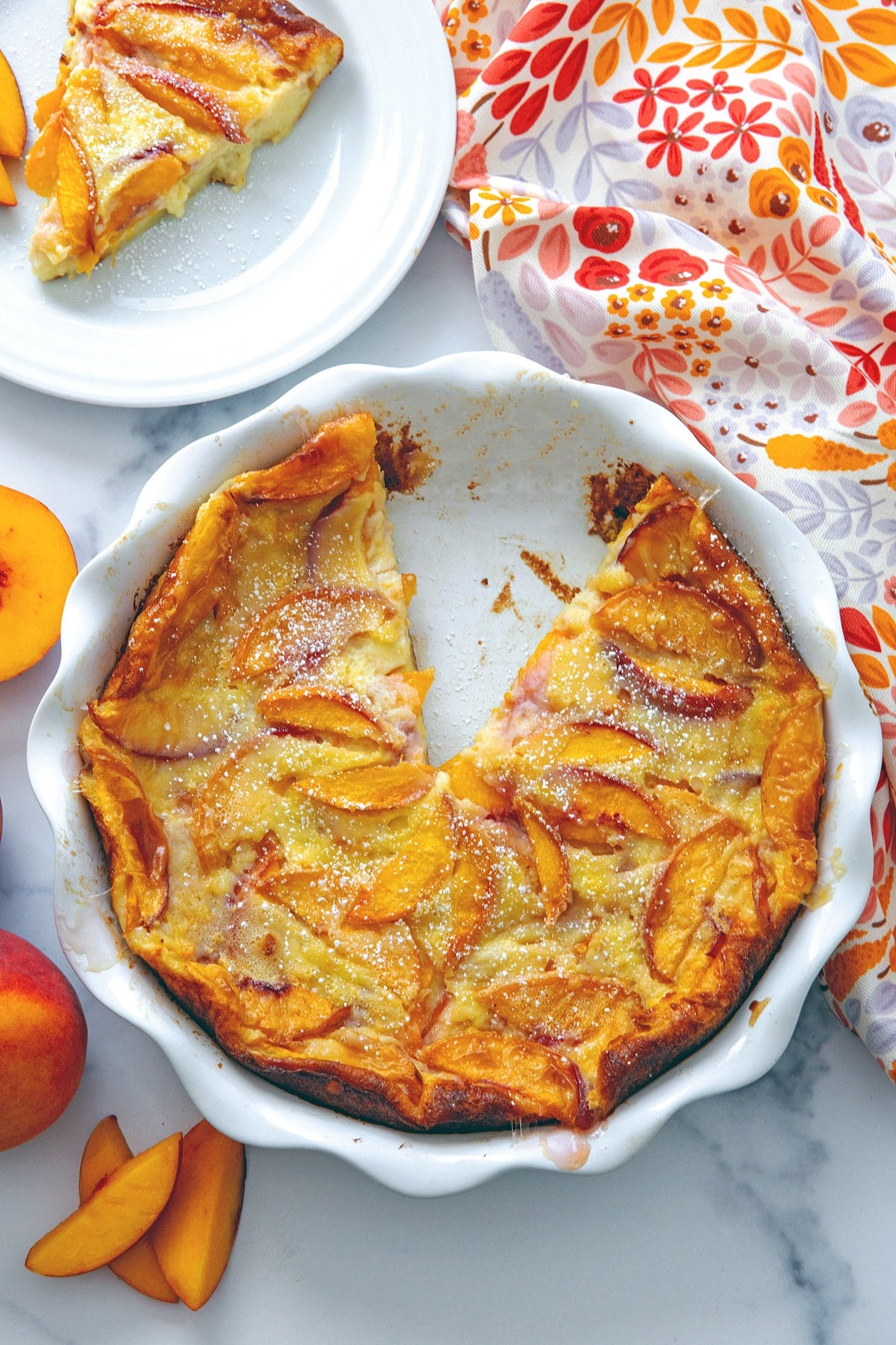 Overhead view of a pie dish of peach clafoutis with a slice taken out.