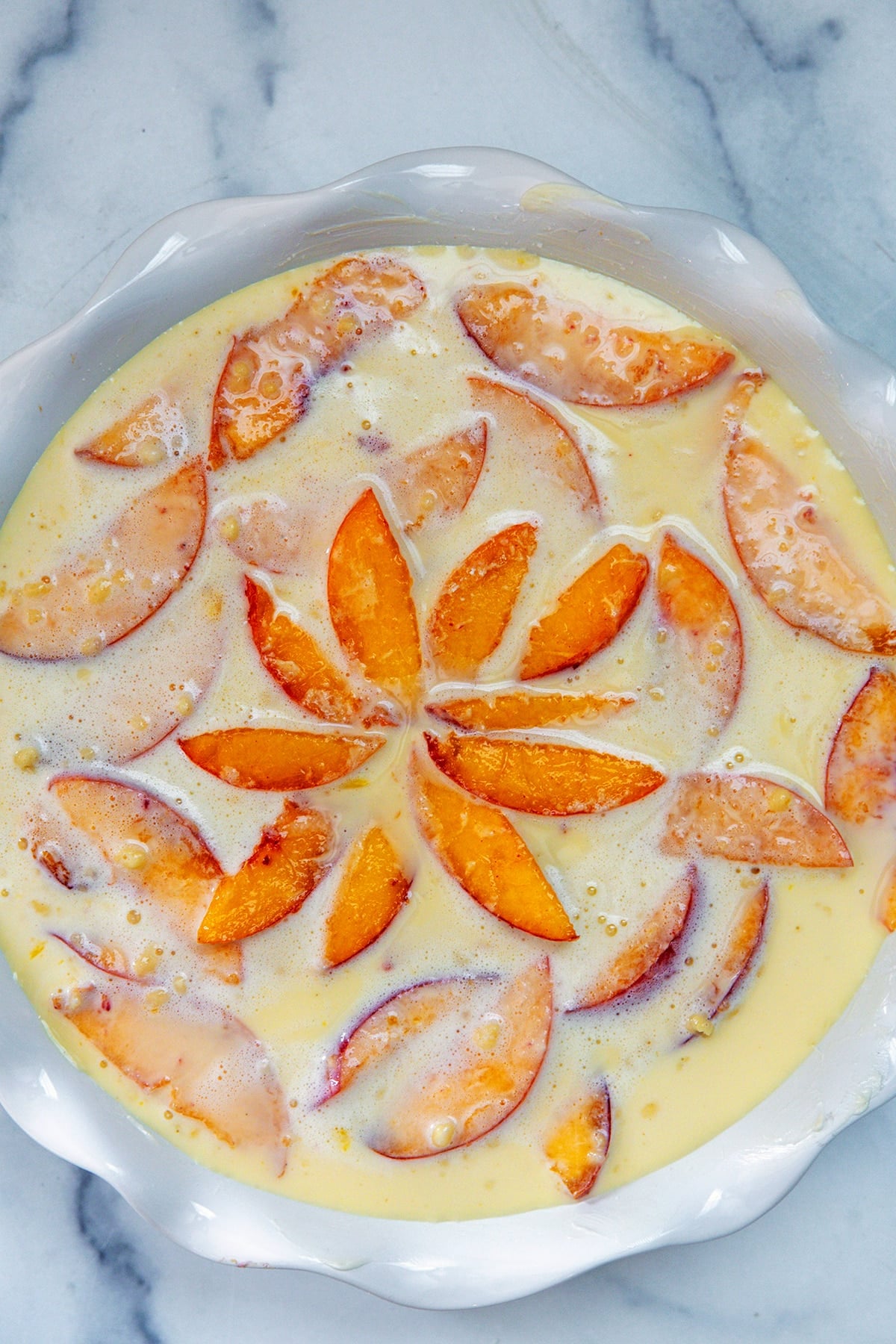 Overhead view of unbaked peach clafoutis in a pie plate.