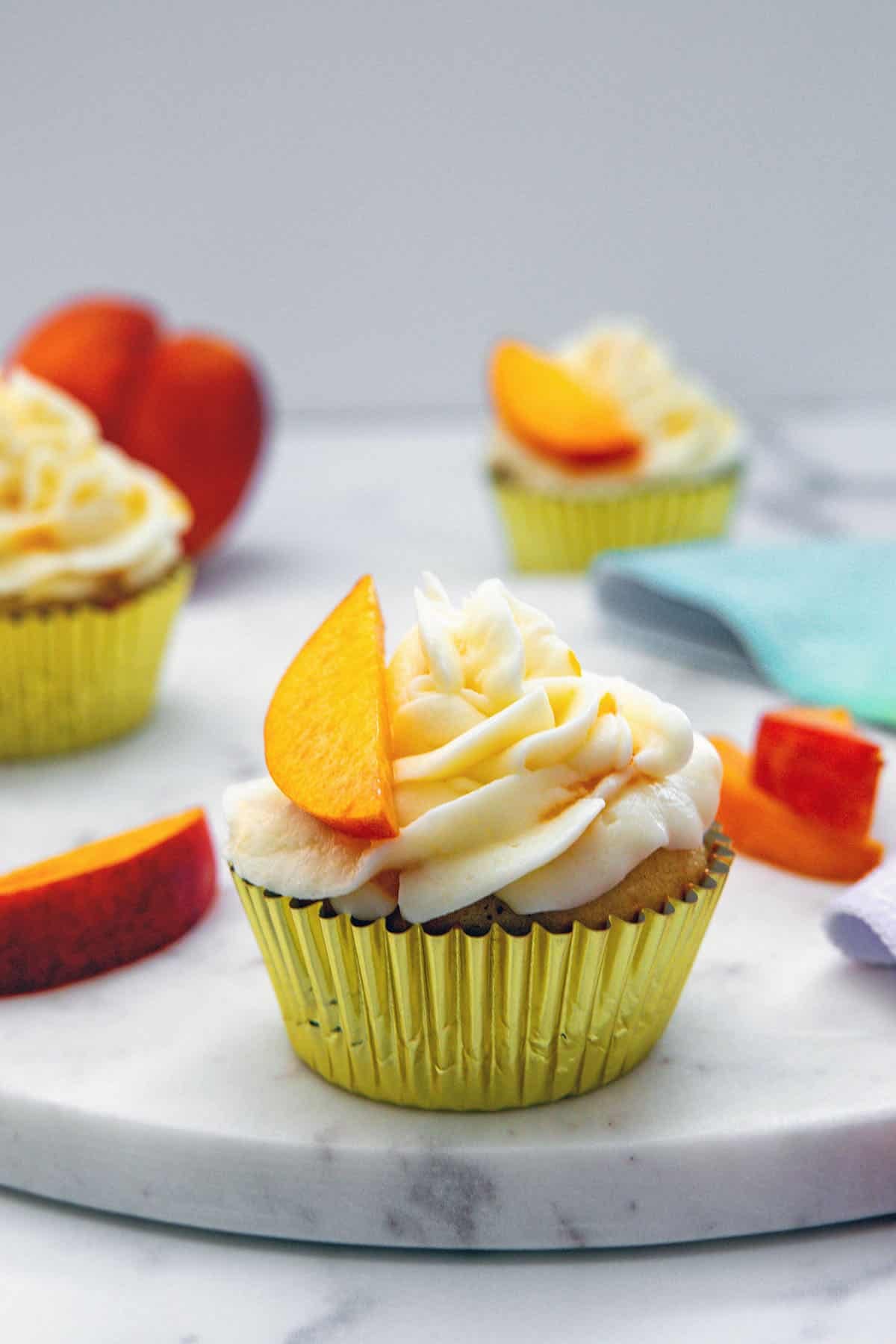 Head-on view of a peach cupcake with more in background and peach slices all round.