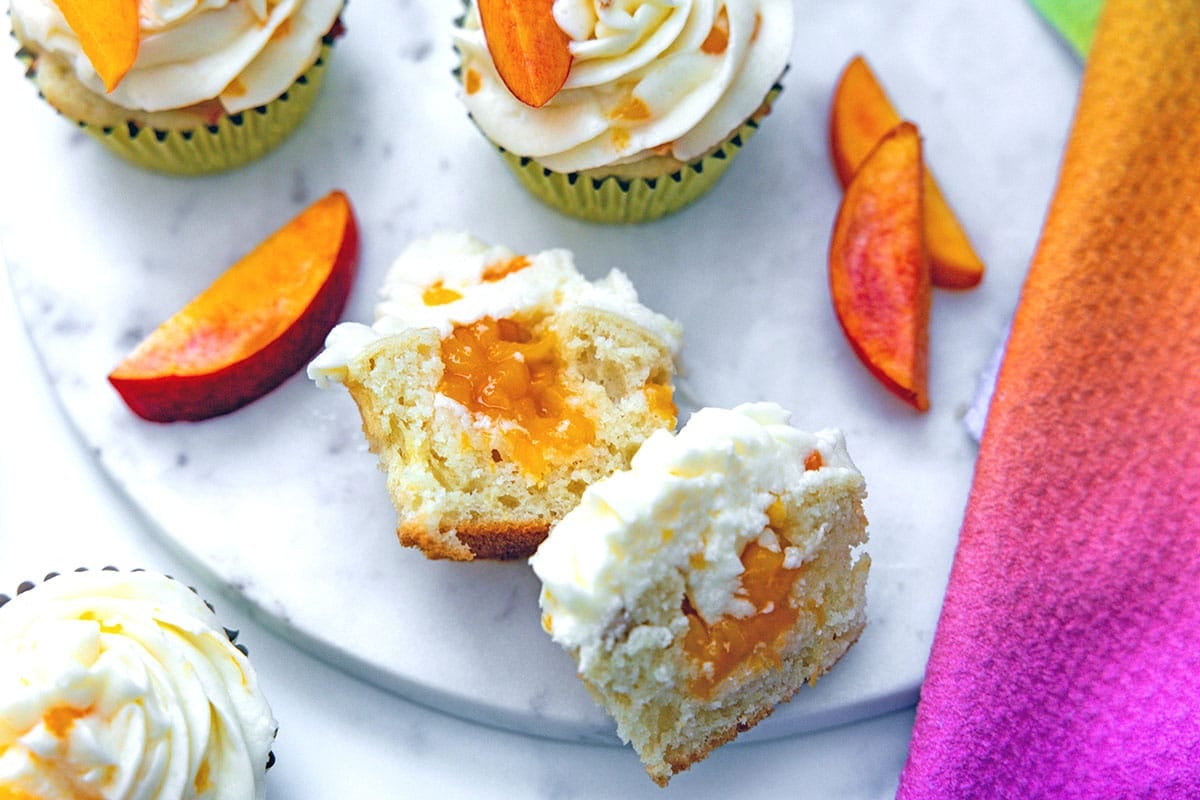 Overhead landscape view of peach cupcakes cut in half to show peach filling inside.