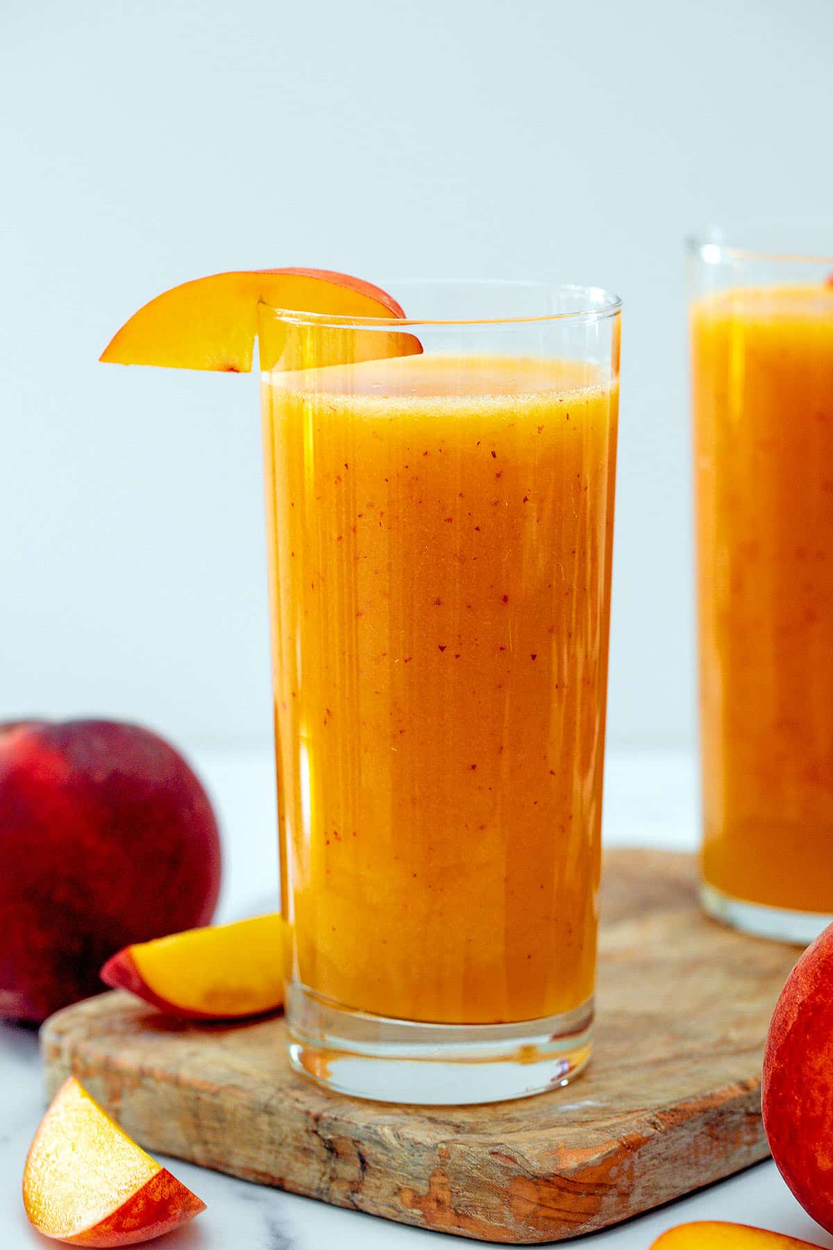 Head-on view of a glass of peach juice with peach slice garnish and peaches all around.