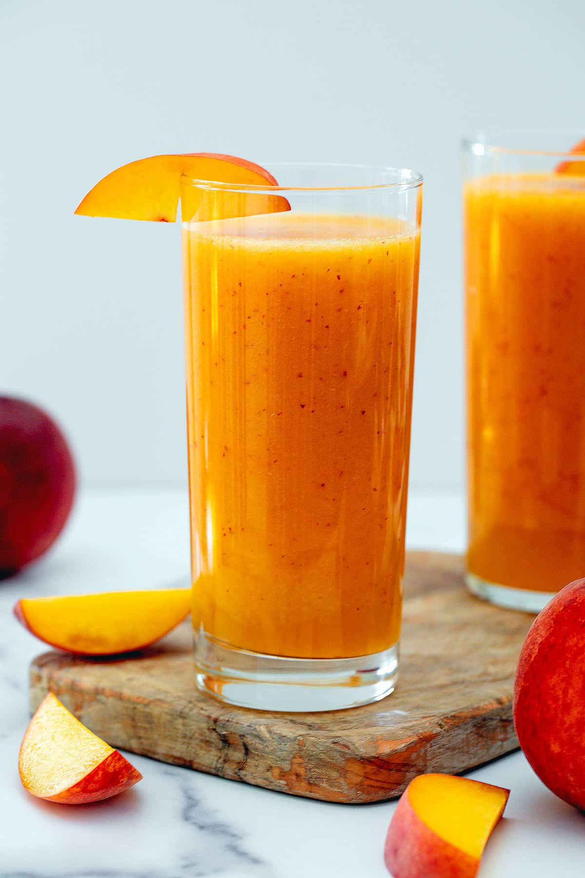 Head-on view of a glass of peach juice with sliced peaches and second glass of juice in background.