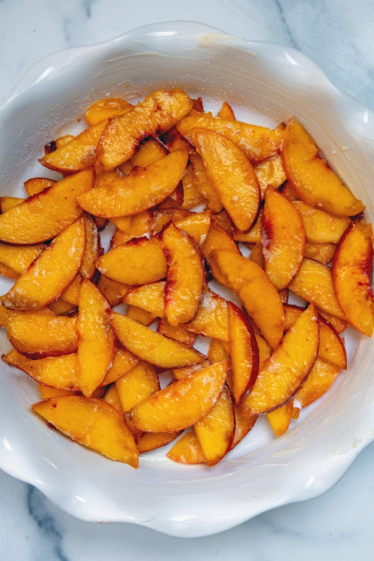 Sliced peaches layered on the bottom of a pie plate.