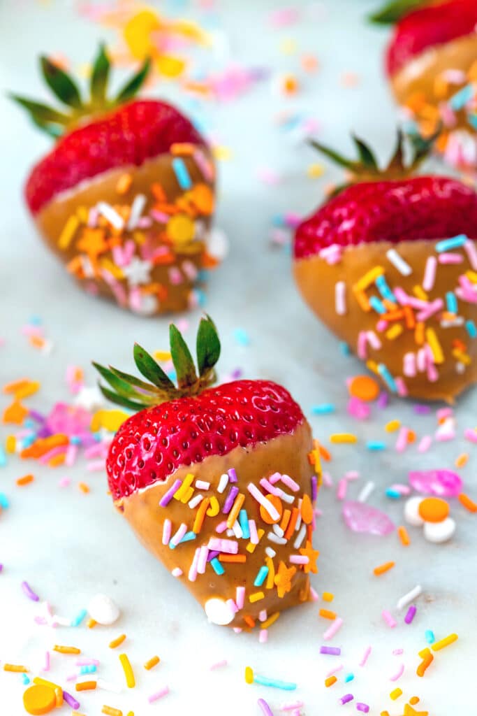 Closeup of peanut butter strawberries with sprinkles all around.